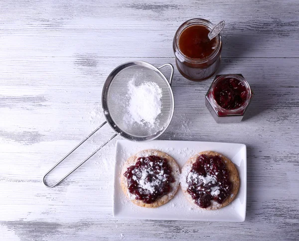 Delicious cookies with jam and powdered sugar on plate on wooden background — Stock Photo, Image