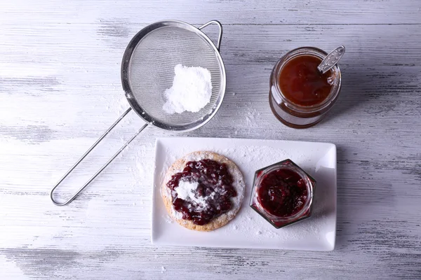 Delicious cookie with jam and powdered sugar on plate on wooden background — Stock Photo, Image