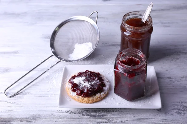 Delicious cookie with jam and powdered sugar on plate on wooden background — Stock Photo, Image