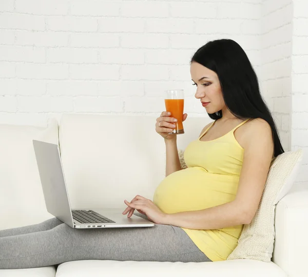 Young pregnant woman relaxing on sofa with laptop on home interior background — Stock Photo, Image