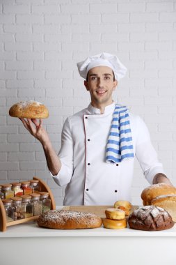 Baker mutfak masasında görmek taze somun ekmek üzerinde beyaz tuğla duvar arka plan