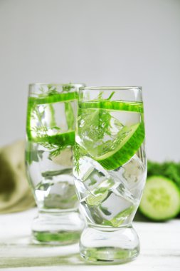 Gri arka planda, ahşap masada taze organik salatalık suyu olan bardaklar.