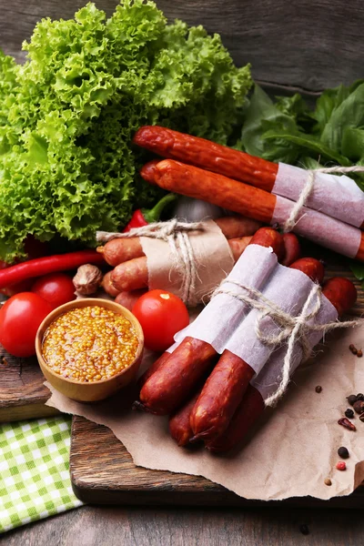 Assortimento di salsicce sottili, senape in ciotola e spezie su tagliere, su fondo di legno — Foto Stock