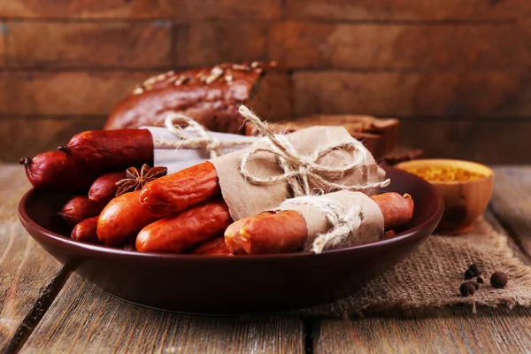 Assortment of thin sausages, and spices on plate, on wooden background — Stock Photo, Image