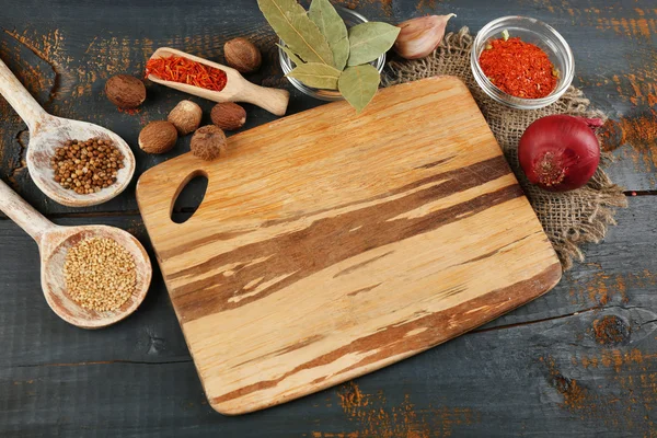 Different spices and herbs with cutting board on color wooden table background — Stock Photo, Image