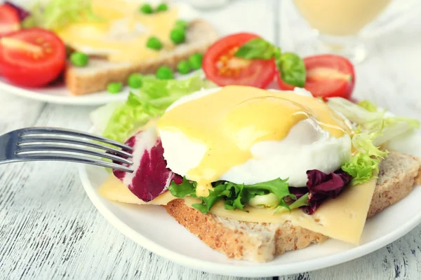 Toast with egg Benedict and tomato on plate on wooden table — Stock Photo, Image