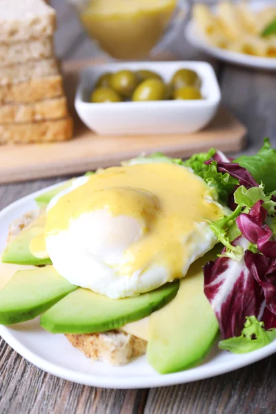 Toast med ägg Benedict och avokado på plattan på träbord — Stockfoto