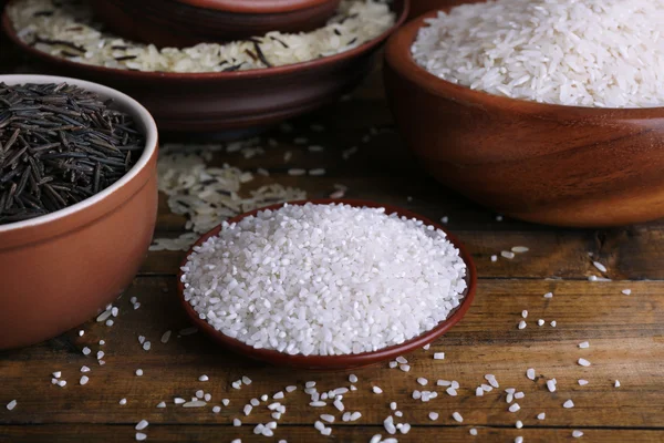 Různé druhy rýže v miskách na dřevěné pozadí — Stock fotografie
