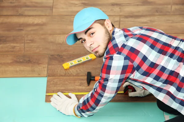 Trabalhador de carpinteiro instalando piso laminado na sala — Fotografia de Stock