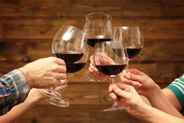 Clinking glasses of red wine in hands on rustic wooden planks background