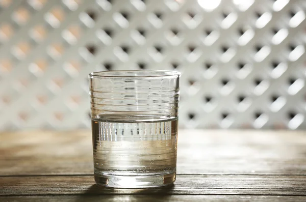 Vetro di acqua minerale pulita su superficie di legno e fondo reticolo — Foto Stock