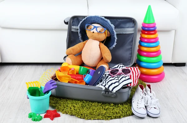 Suitcase packed with clothes and child toys on fur rug and white sofa background — Stock Photo, Image