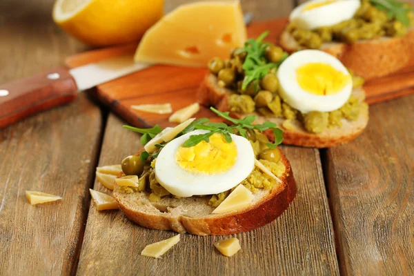 Sandwiches with green peas paste and boiled egg with cutting board on wooden planks background — Stock Photo, Image