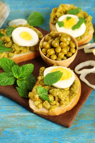 Sandwiches with green peas paste and boiled egg with napkin on color wooden background — Stock Photo, Image