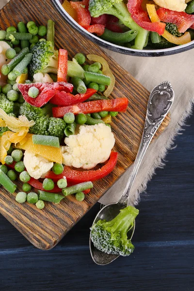 Légumes congelés sur planche à découper, sur serviette, sur fond de table en bois — Photo