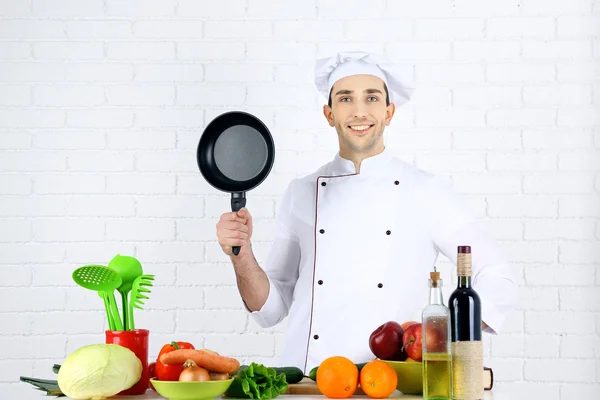 Chef à mesa com diferentes produtos e utensílio na cozinha no fundo da parede branca — Fotografia de Stock