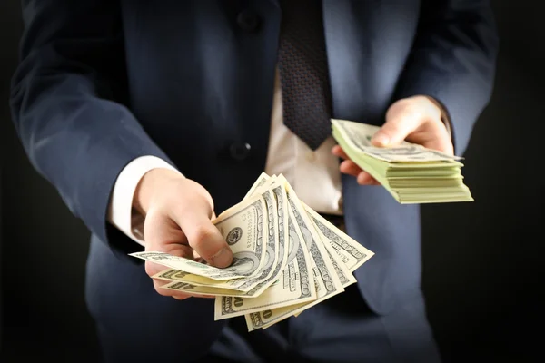 Businessman giving money on dark background — Stock Photo, Image