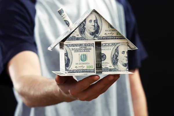 Model of house made of money in male hands on dark background — Stock Photo, Image