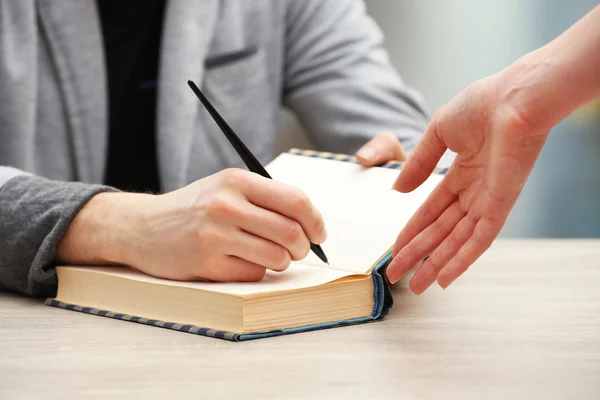 Author signing autograph in own book at wooden table on light blurred background