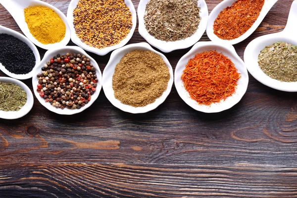 Different kinds of spices in ceramics bowls and spoons on wooden background — Stock Photo, Image