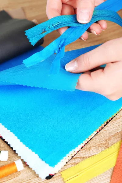 Muestras de tela coloridas y cremallera en manos femeninas sobre fondo de mesa de madera —  Fotos de Stock