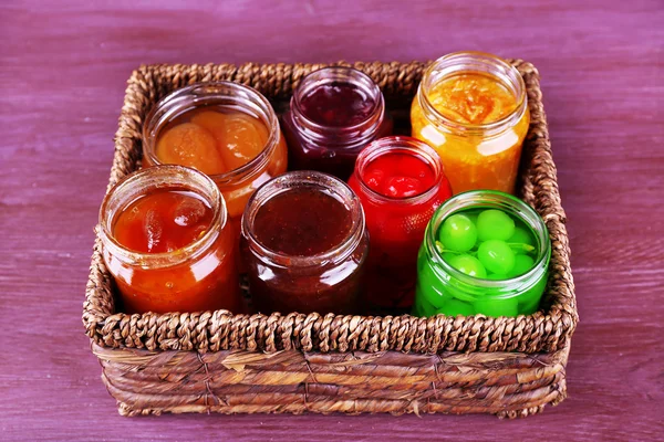 Zelfgemaakte potten van vruchten jam in rieten mand en kleur houten achtergrond — Stockfoto