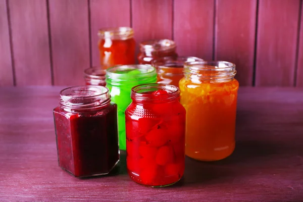 Homemade jars of fruits jam on color wooden background — Stock Photo, Image