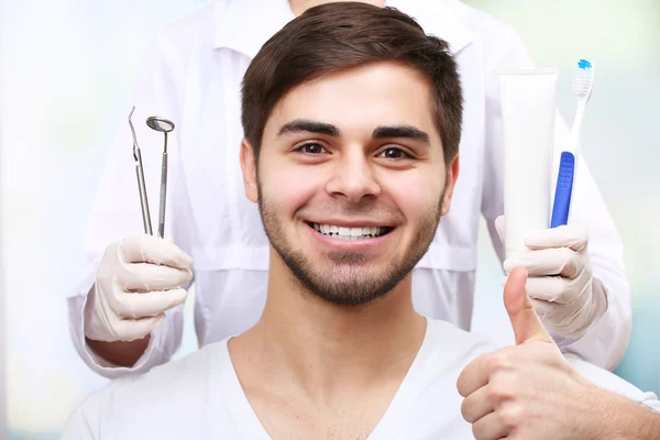 Examen de hombre joven por dentista sobre fondo borroso claro — Foto de Stock