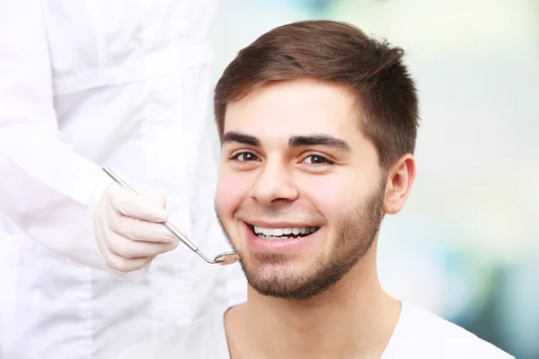 Zbadać młodego człowieka przez stomatologa na jasnym tle niewyraźne — Zdjęcie stockowe