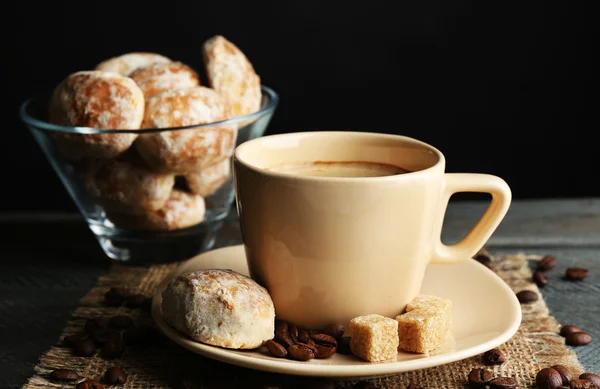 Tazza di caffè e biscotti gustosi su tovagliolo di sacco, su tavolo di legno, su sfondo scuro — Foto Stock