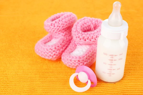 Baby milk bottle, pacifier and babys bootees on yellow background — Stock Photo, Image