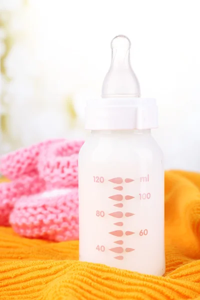 Baby milk bottle and babys bootees on yellow background — Stock Photo, Image