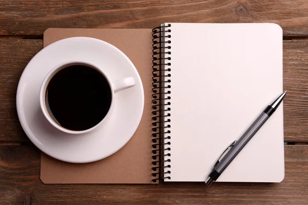 Xícara de café em pires com notebook e caneta sobre fundo de mesa de madeira — Fotografia de Stock