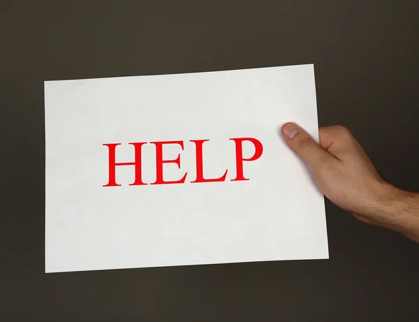 Sheet of paper with Help sign in male hand on dark background — Stock Photo, Image