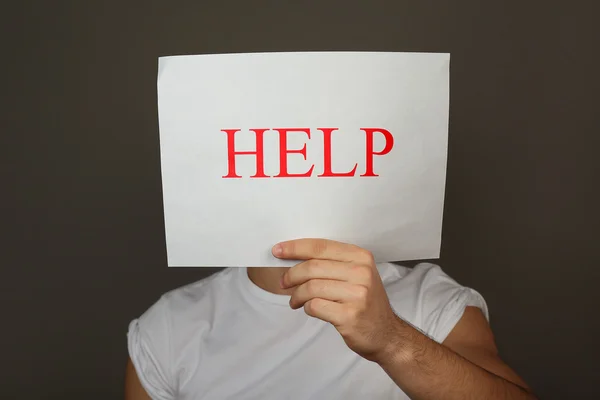 Sheet of paper with Help sign in male hand on dark background — Stock Photo, Image