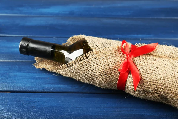 Vinflaska insvept i säckväv tyg på träplankor färgbakgrund — Stockfoto