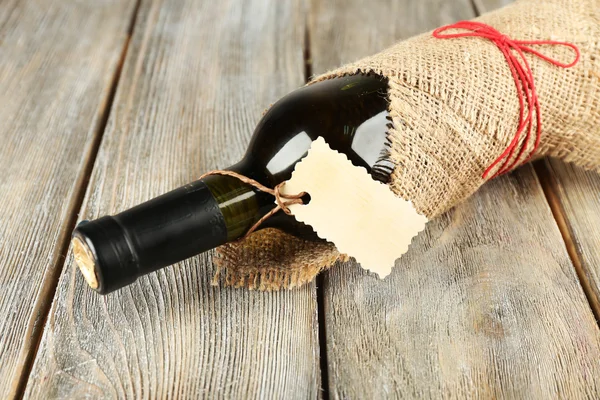 Şarap şişesi ahşap plakalar arka plan üzerine çuval bezi kumaş sarılmış — Stok fotoğraf