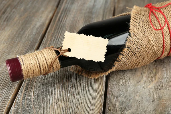 Bouteille de vin rouge enveloppée dans un tissu de toile de jute sur des planches en bois — Photo