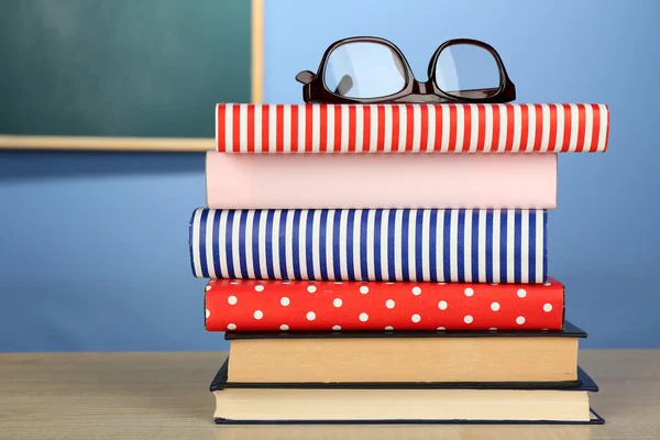 Montón de libros con gafas sobre escritorio de madera, sobre pared colorida y fondo de pizarra —  Fotos de Stock