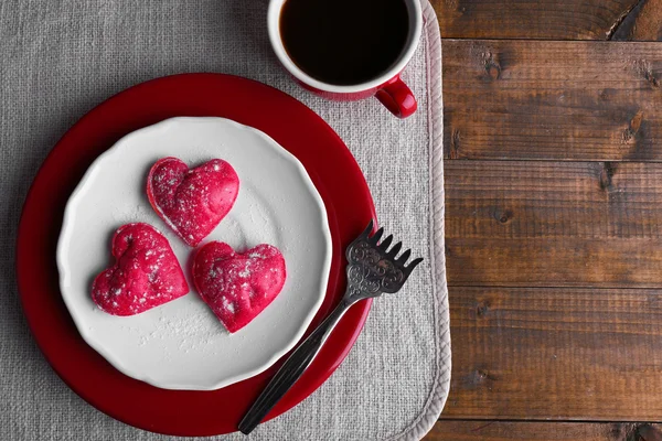 Biscotti in forma di cuore in piatto con tazza di caffè sul tovagliolo, su tavole di legno rustico sfondo — Foto Stock