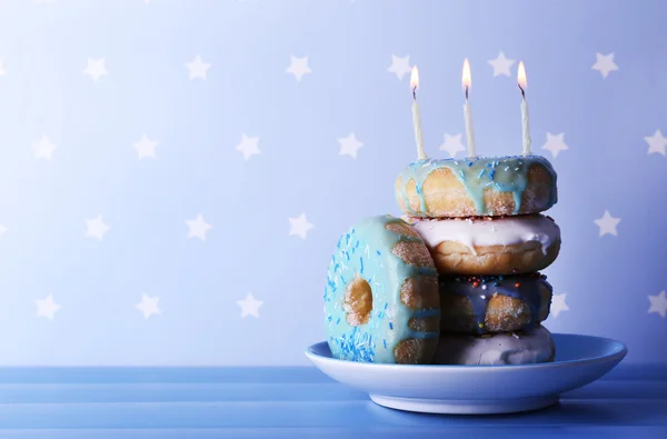 Delicious donuts with icing and birthday candles on table on bright background — Stock Photo, Image