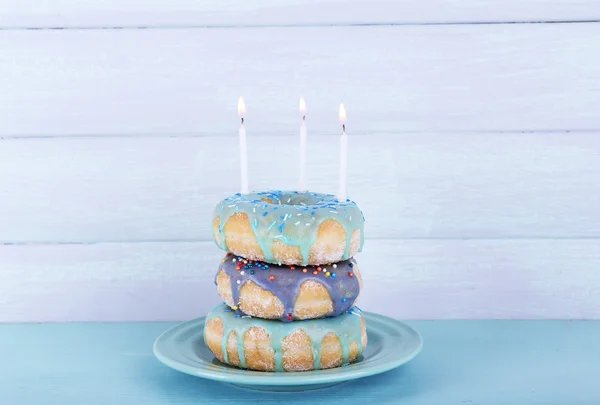 Herkullisia donitseja kuorrutuksella ja syntymäpäiväkynttilöillä pöydällä puupohjalla — kuvapankkivalokuva