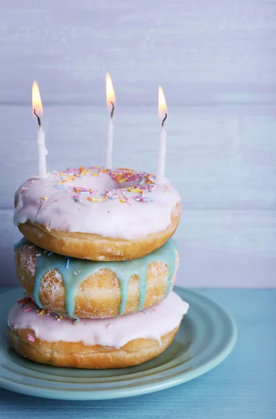 Delicious donuts with icing and birthday candles on table on wooden background — Stock Photo, Image