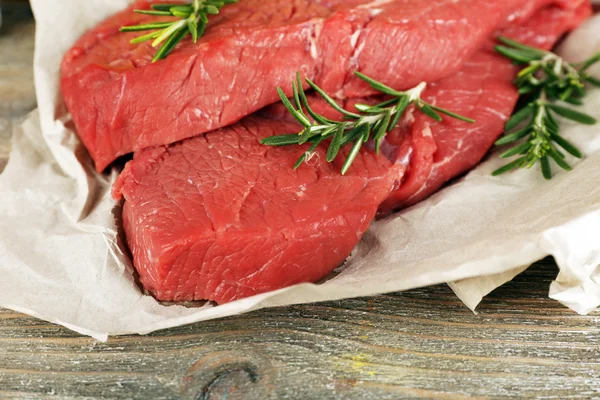 Raw beef steak with rosemary on paper on wooden background — Stock Photo, Image