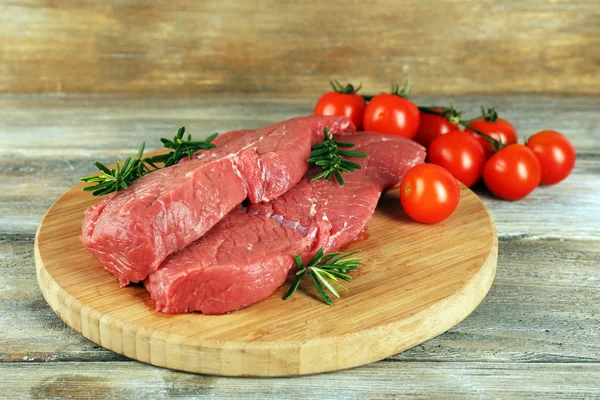 Bistecca di manzo cruda con rosmarino e pomodorini su tagliere su fondo di legno — Foto Stock