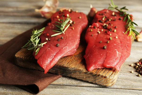 Bistecca di manzo cruda con rosmarino e spezie sul tagliere su fondo di legno — Foto Stock