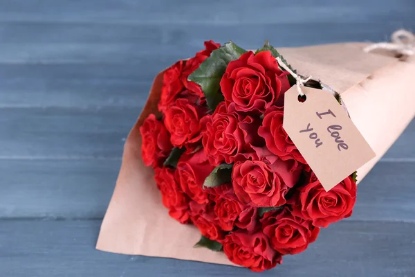 Ramo de rosas rojas con etiqueta envuelta en papel sobre fondo de madera — Foto de Stock