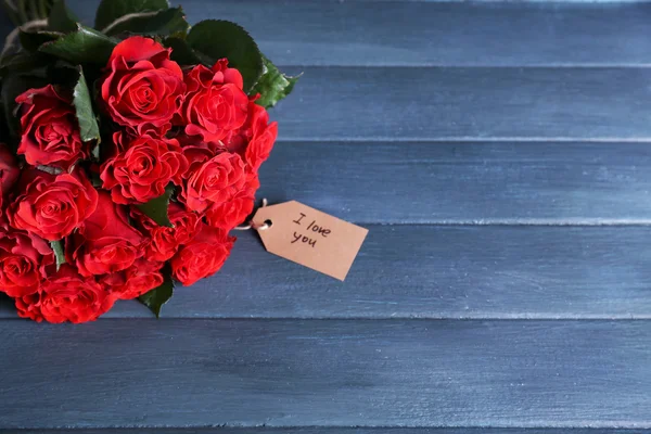 Ramo de rosas rojas con etiqueta sobre fondo de madera —  Fotos de Stock