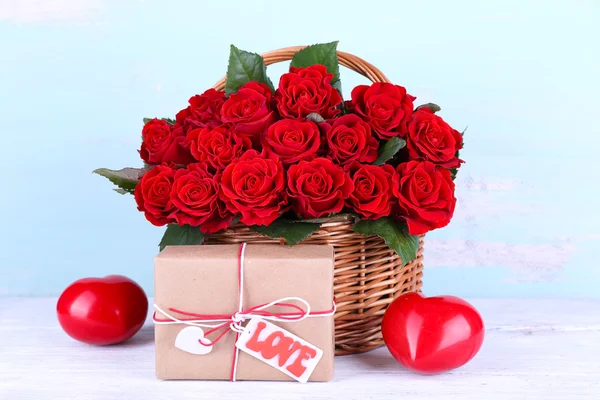 Bouquet of red roses in basket with present box on wooden background — Stock Photo, Image