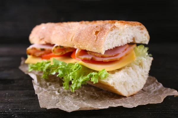 Fresh and tasty sandwich with ham and vegetables on paper on wooden background — Stock Photo, Image
